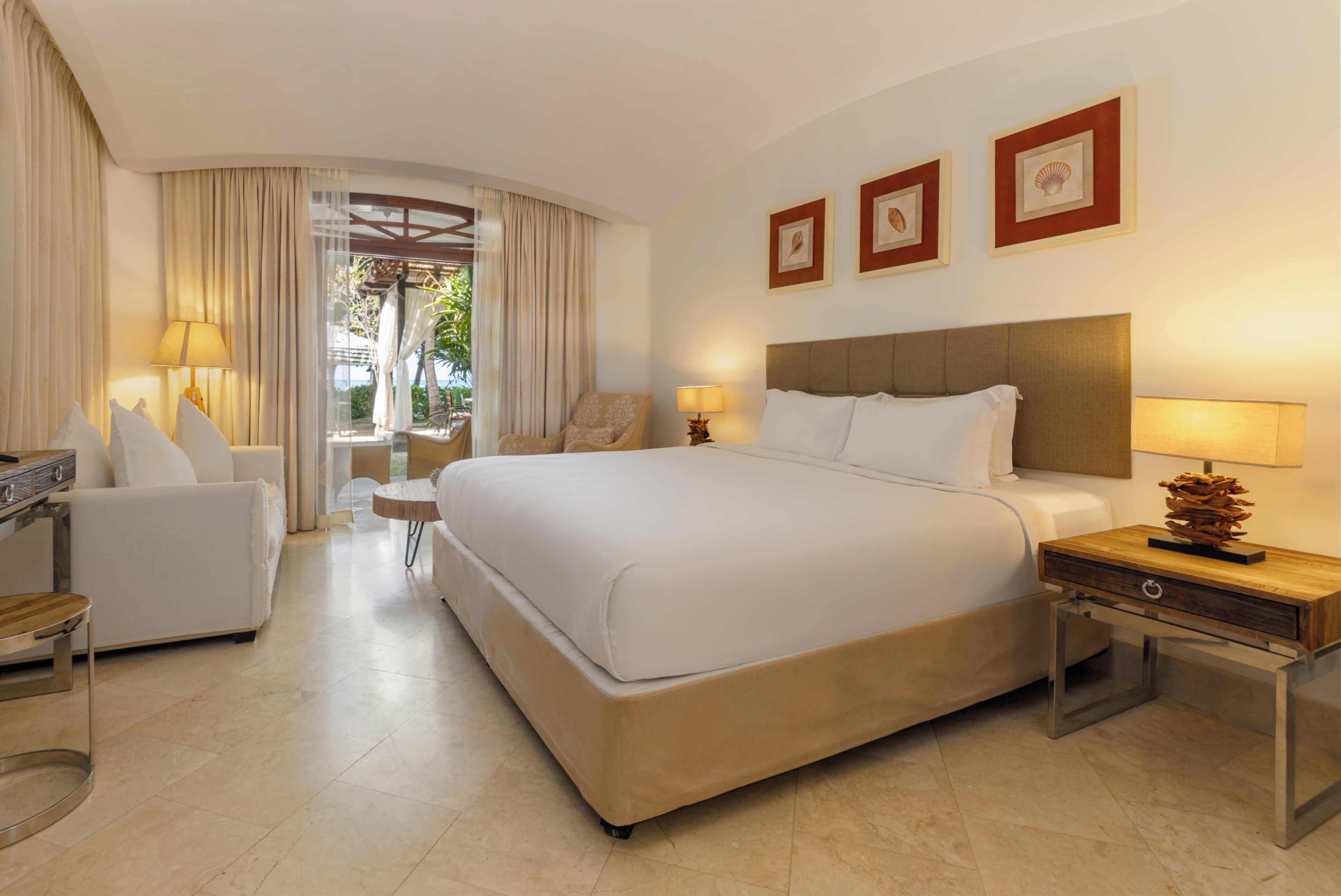Una habitación de hotel con una cama grande, un sofá, una silla, una mesita y una lámpara.