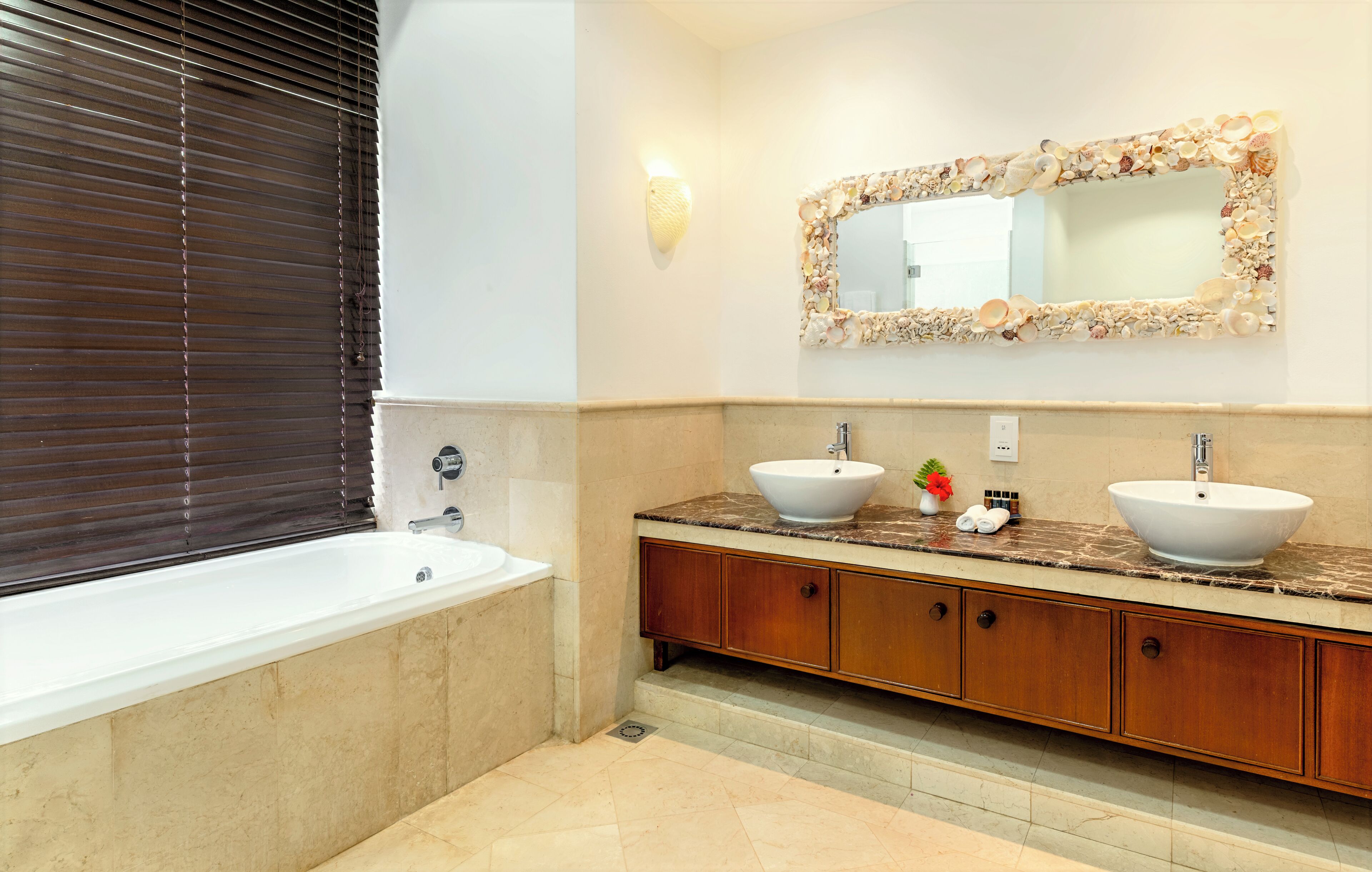 Un bagno con vasca, due lavandini, un mobile vanitario con specchio e un fiorileto a parete.