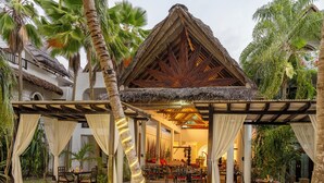 A resort with outdoor seating, a thatched-roof structure, and palm trees. - Village Du Pecheur (Praslin Island)