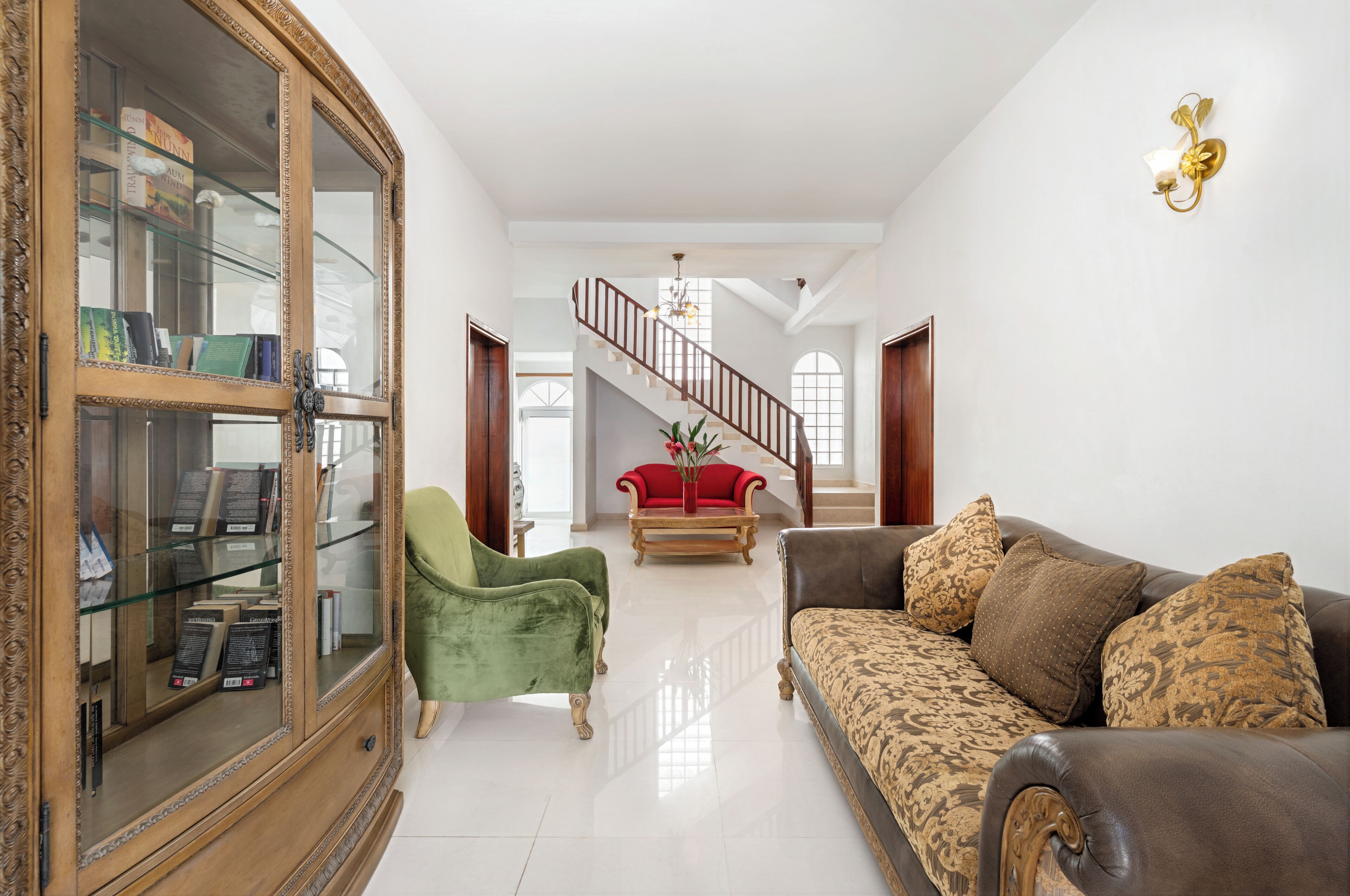 Uma sala de estar ampla com uma escada, uma poltrona verde, um sofá vermelho e um sofá estampado.
