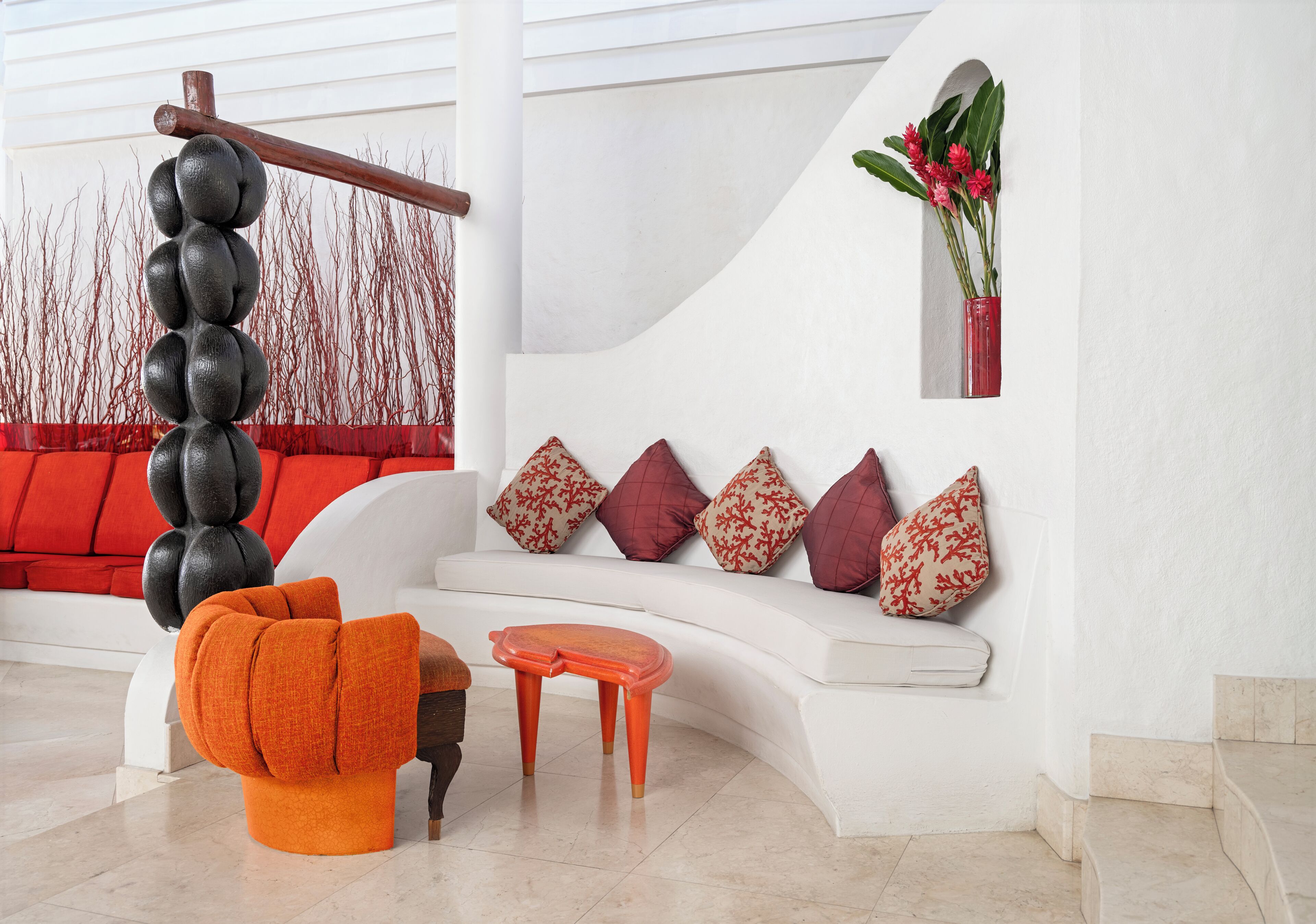 A modern living room with a white sofa, orange armchair, and a unique black and orange sculpture.