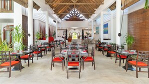 A spacious indoor dining area with wooden tables and chairs, large windows, and a high ceiling with wooden beams. - Village Du Pecheur (Praslin Island)