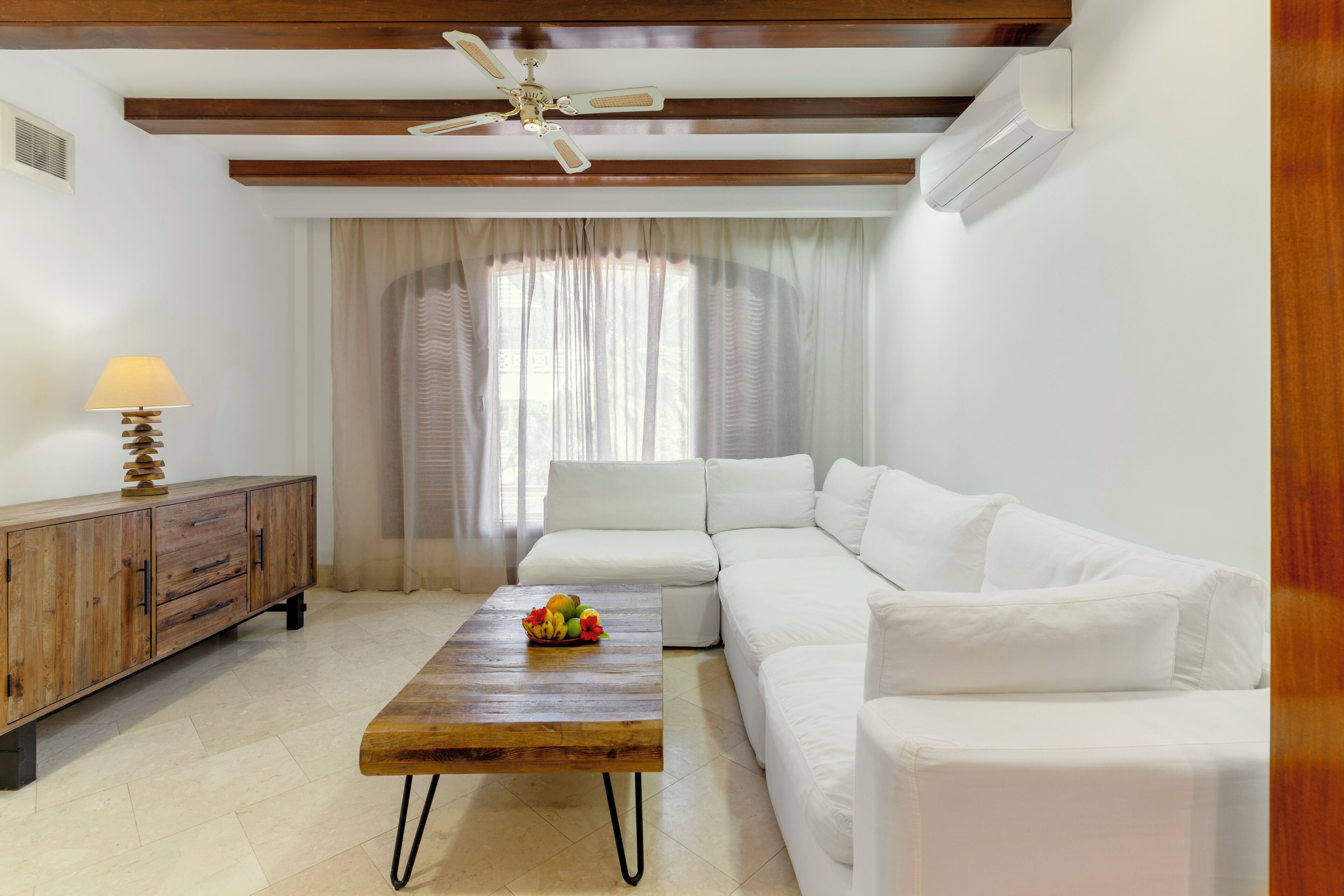 Una sala de estar con una mesa de centro de madera, sofá blanco, ventilador de techo y un mueble de madera.