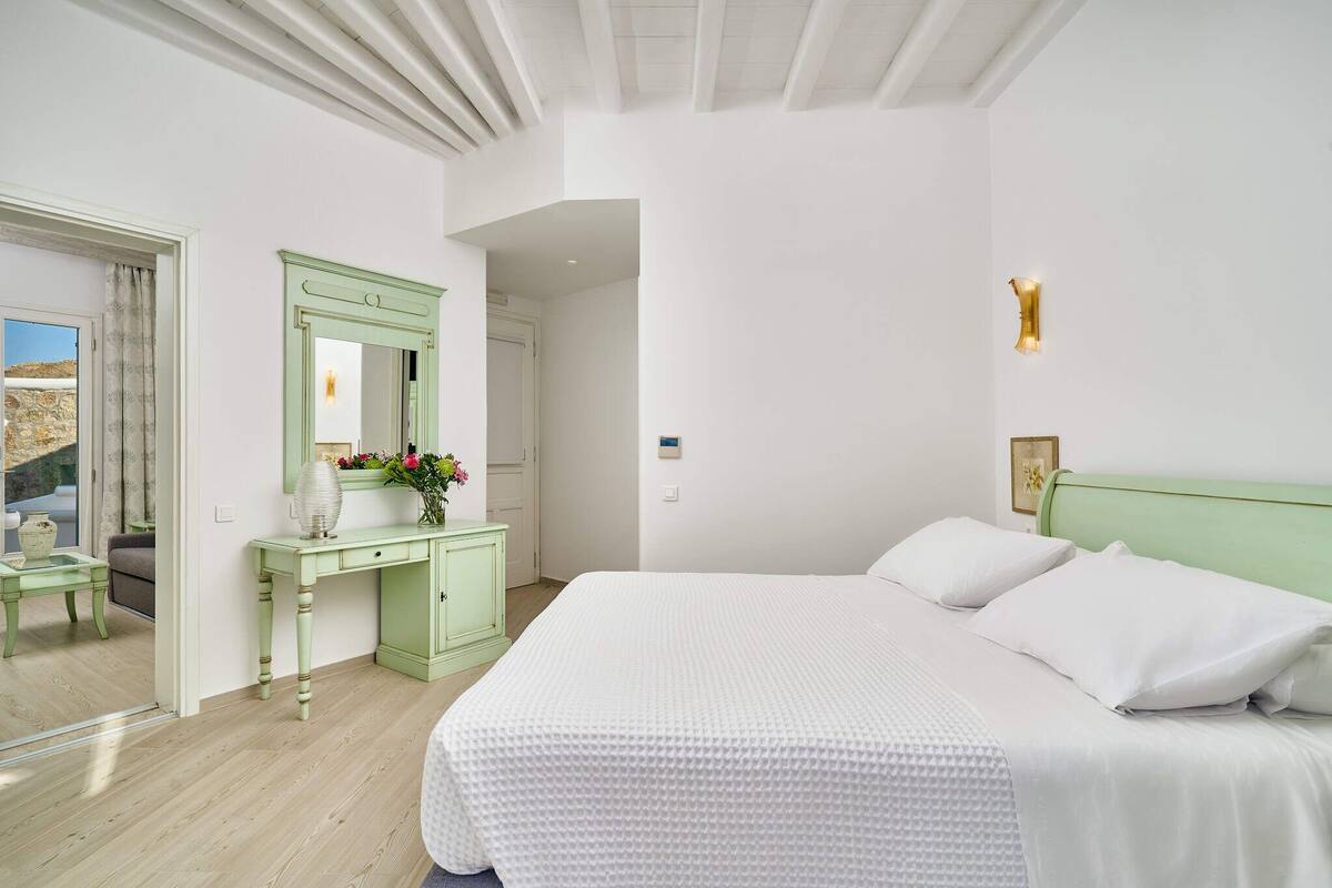 Une chambre à coucher avec un grand lit, une coiffeuse verte, un miroir et un luminaire fixé au mur.