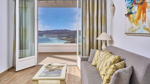 A living room with a grey sofa, a glass coffee table, and a view of the sea through an open door.