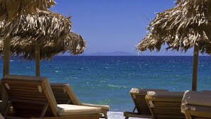 A beach with wooden lounge chairs and thatched umbrellas.