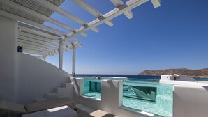 A modern outdoor balcony with a clear view of the sea, a white staircase, and a glass-enclosed pool area.