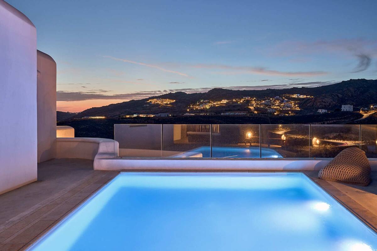 Une piscine sur le toit offrant une vue sur une ville côtière illuminée au crépuscule.
