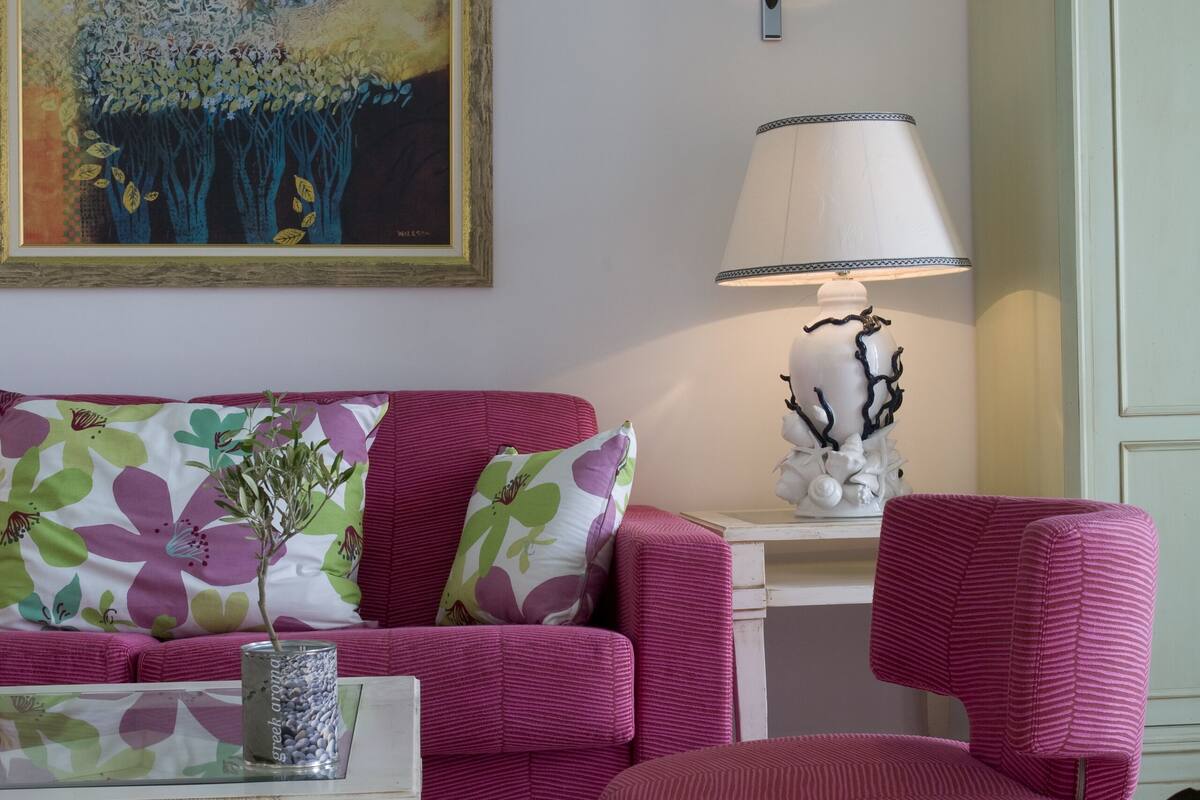 Un salon avec un canapé, un fauteuil rond de couleur rose, une table basse, une lampe et un tableau accroché au mur.
