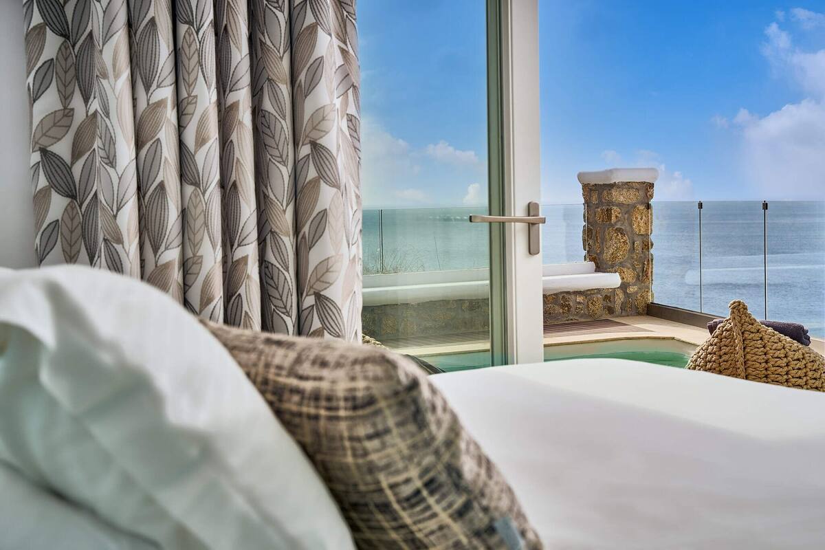 Une chambre avec une grande fenêtre donnant sur une piscine et l’océan.