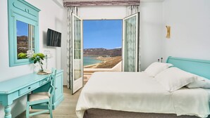 A bedroom with a bed, a desk, and a view of the sea.