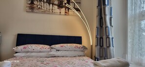Un lit bien fait, avec une literie à motifs floraux, une tête de lit sombre et un luminaire fixé au mur.
