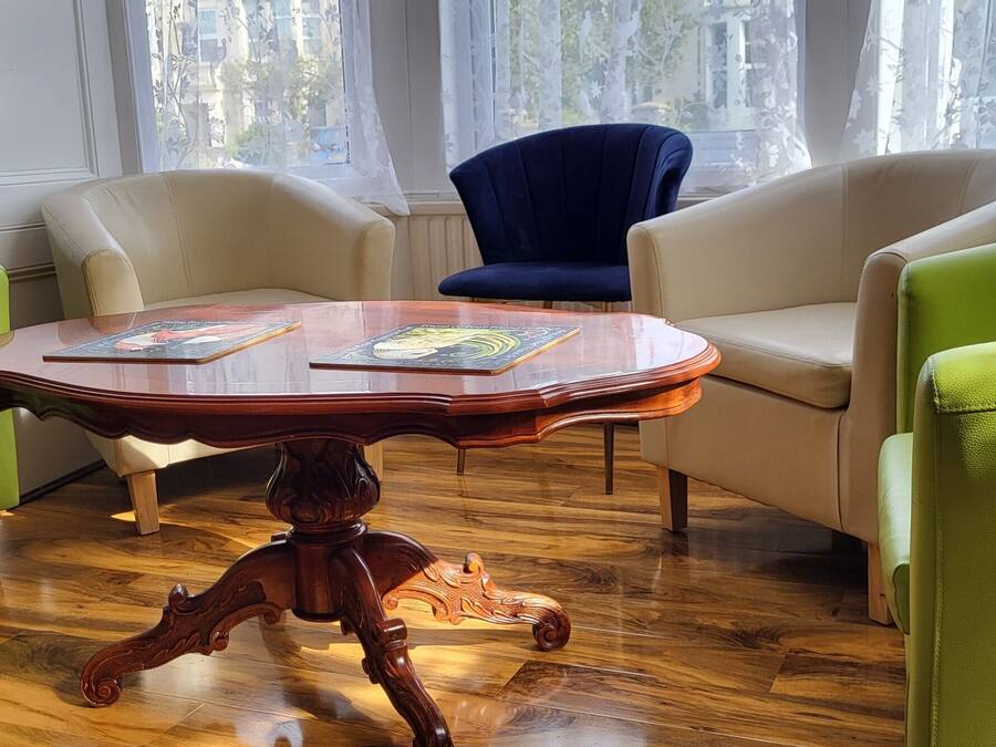 Ein Zimmer mit einem Holztisch, zwei grünen Sesseln und einem blauen Stuhl.
