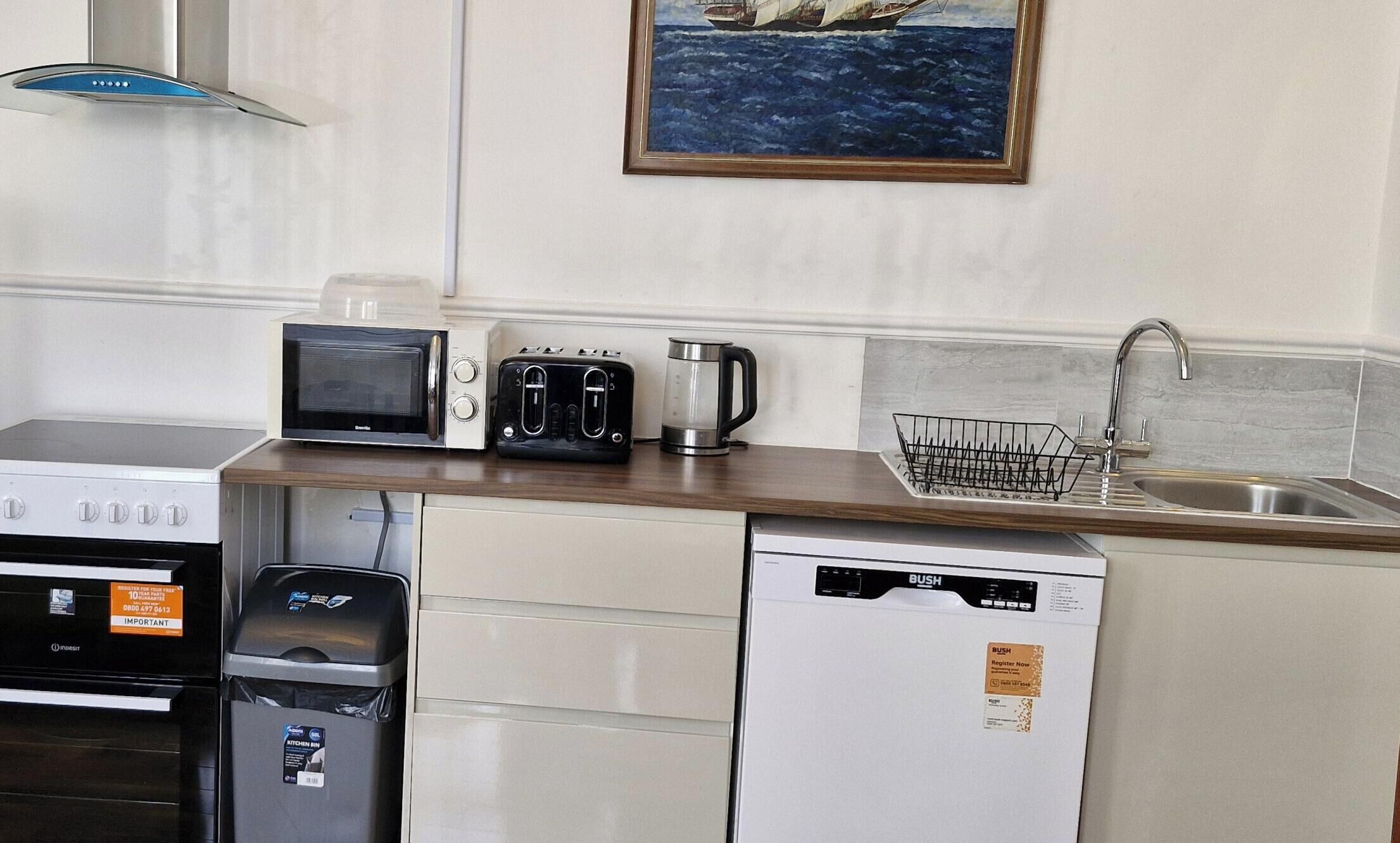 A compact kitchenette with a microwave, toaster, coffee maker, and a dish rack.