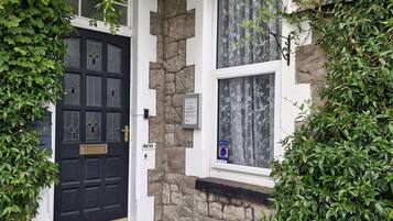 A black door with a brass handle, a stone wall, and a window with floral curtains.