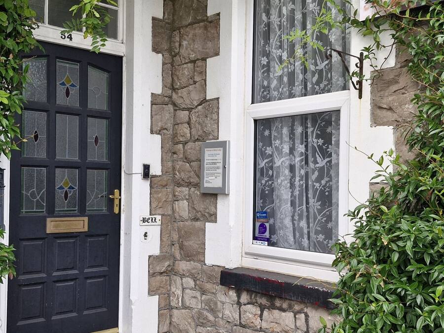 A black door with a brass handle, a stone wall, and a window with floral curtains.