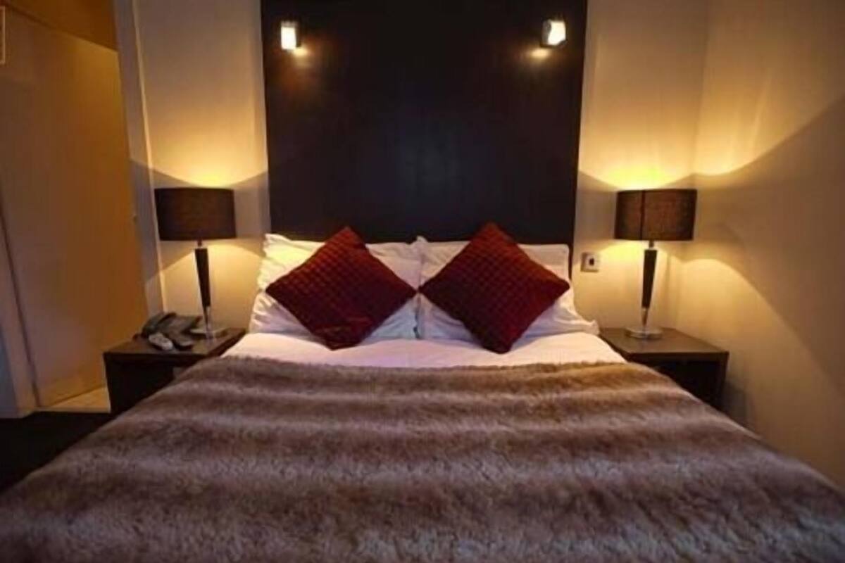 A hotel room with a large bed, two bedside lamps, a telephone, and a dark headboard.