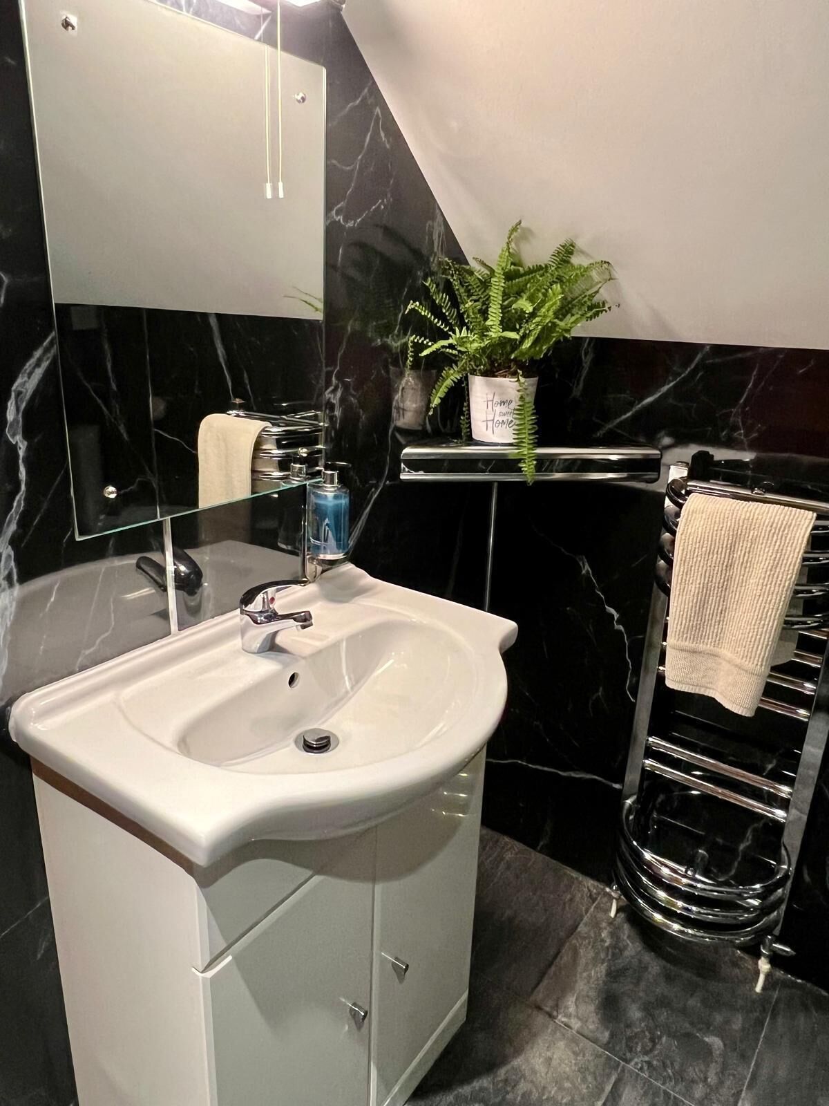 A bathroom with a white sink, a mirror, a potted plant, and a towel rack.