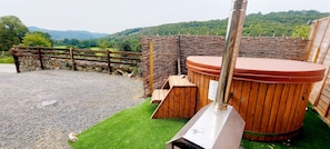 A hot tub area with a stone wall, wooden fence, and a view of green hills. - Dolgun Uchaf Guesthouse (Dolgellau)