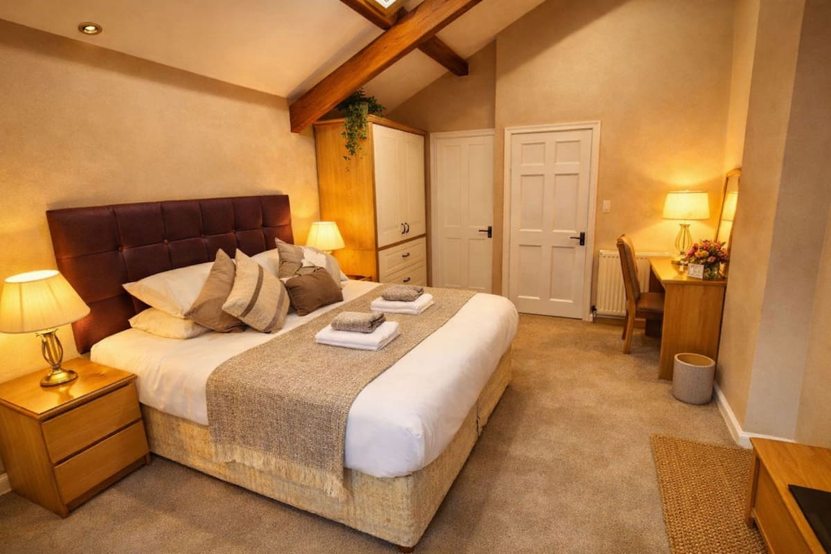 Un dormitorio con una cama grande, mesitas de noche con lámparas, un armario de madera, un escritorio con silla y una puerta.