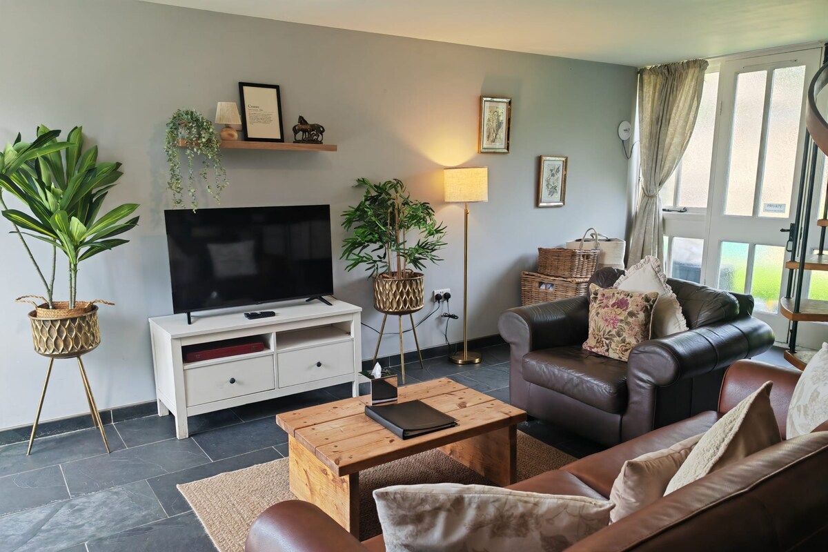 Een woonkamer met een leren bank, een flatscreen televisie, een houten salontafel en potplanten.