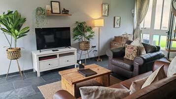 A living room with a leather sofa, a flat-screen TV, a wooden coffee table, and potted plants.