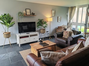 A living room with a leather sofa, a flat-screen TV, a wooden coffee table, and potted plants. - Dolgun Uchaf Guesthouse (Dolgellau)