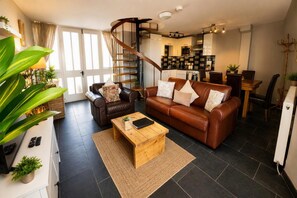 A modern living room with a brown leather sofa, a wooden coffee table, and a spiral staircase leading to a kitchen. - Dolgun Uchaf Guesthouse (Dolgellau)