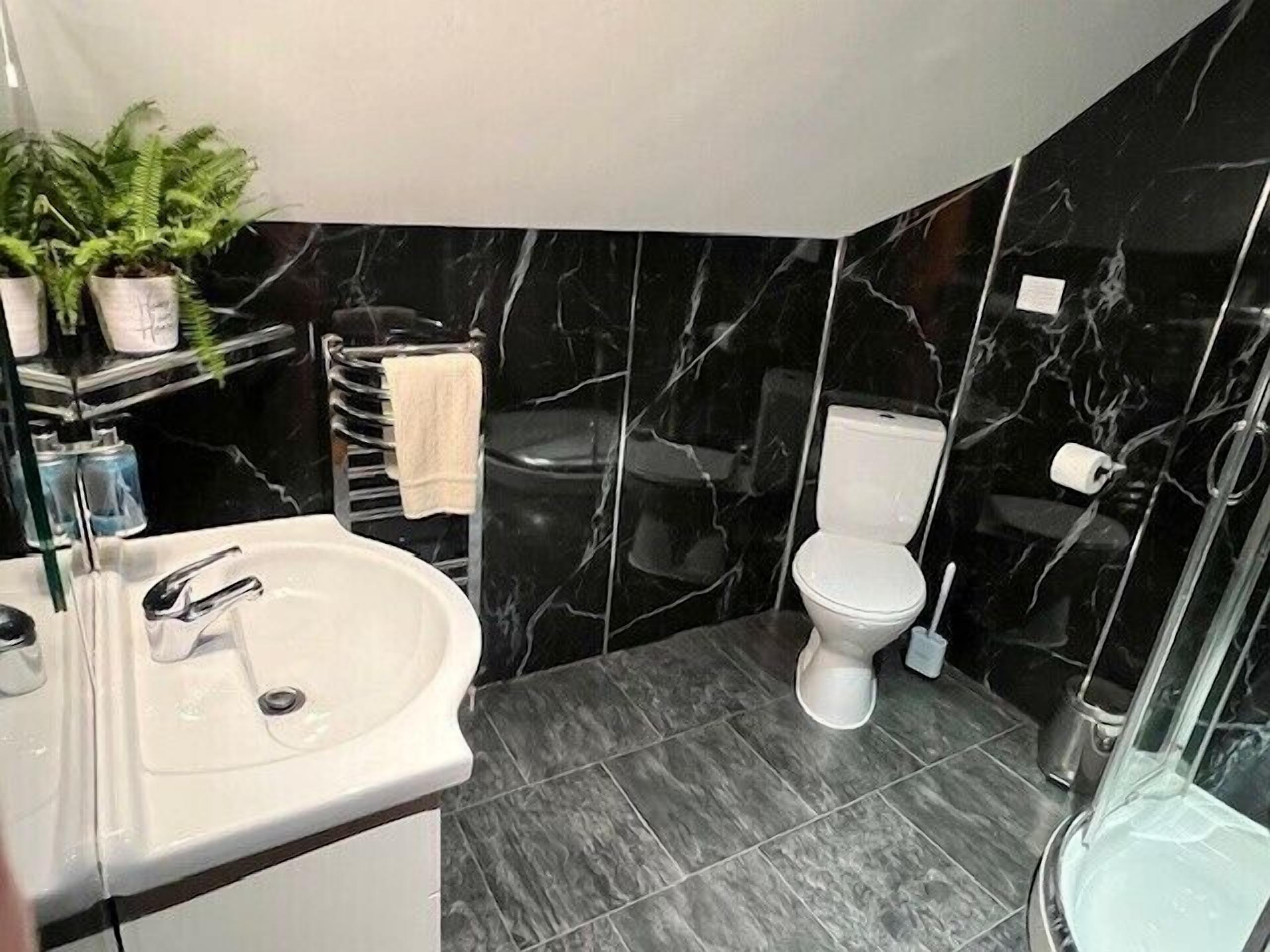 Une salle de bain moderne avec un lavabo blanc, des murs en marbre noir, des toilettes blanches et une cabine de douche en verre.