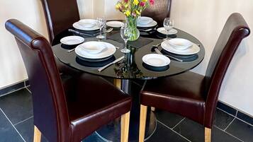 Una mesa de comedor redonda con platos blancos y negros, un florero con flores y sillas de cuero marrón oscuro.