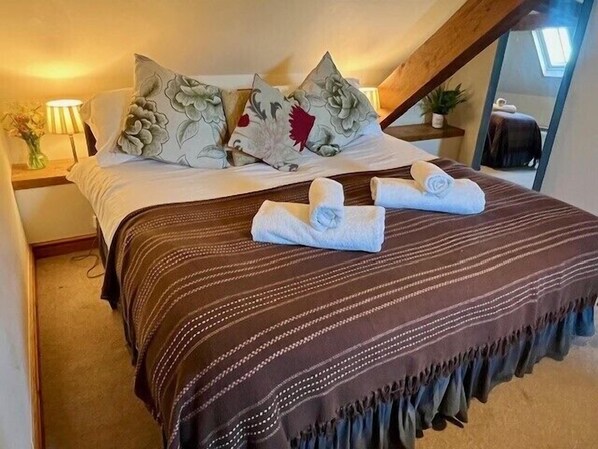 A bedroom with a bed, pillows, a striped blanket, and rolled towels on the bed. - Dolgun Uchaf Guesthouse (Dolgellau)