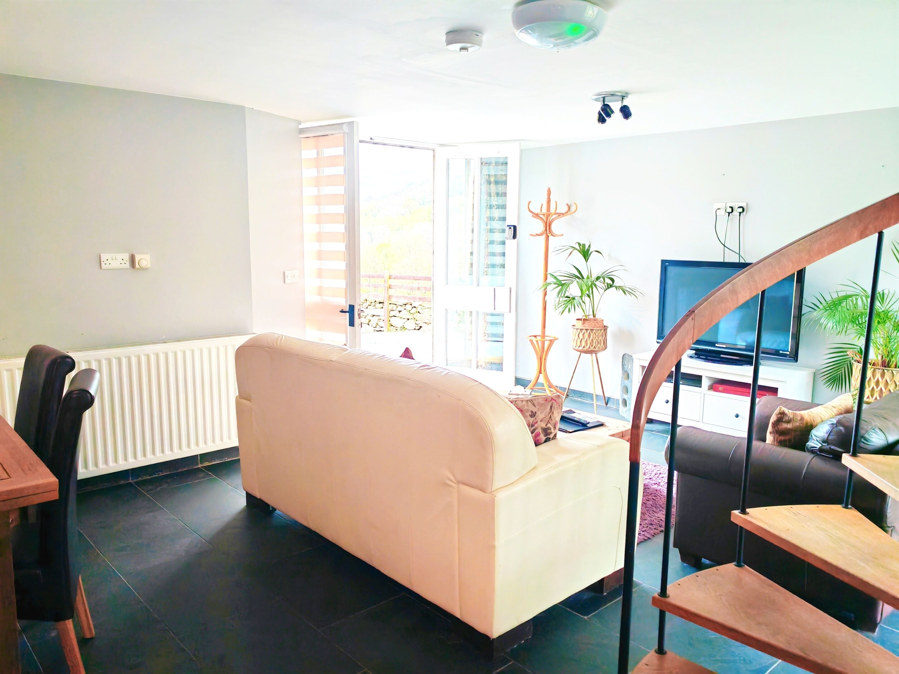 A living room with a sofa, a dining table with chairs, a TV, and a staircase.