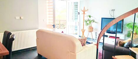 A living room with a sofa, a dining table with chairs, a TV, and a staircase.