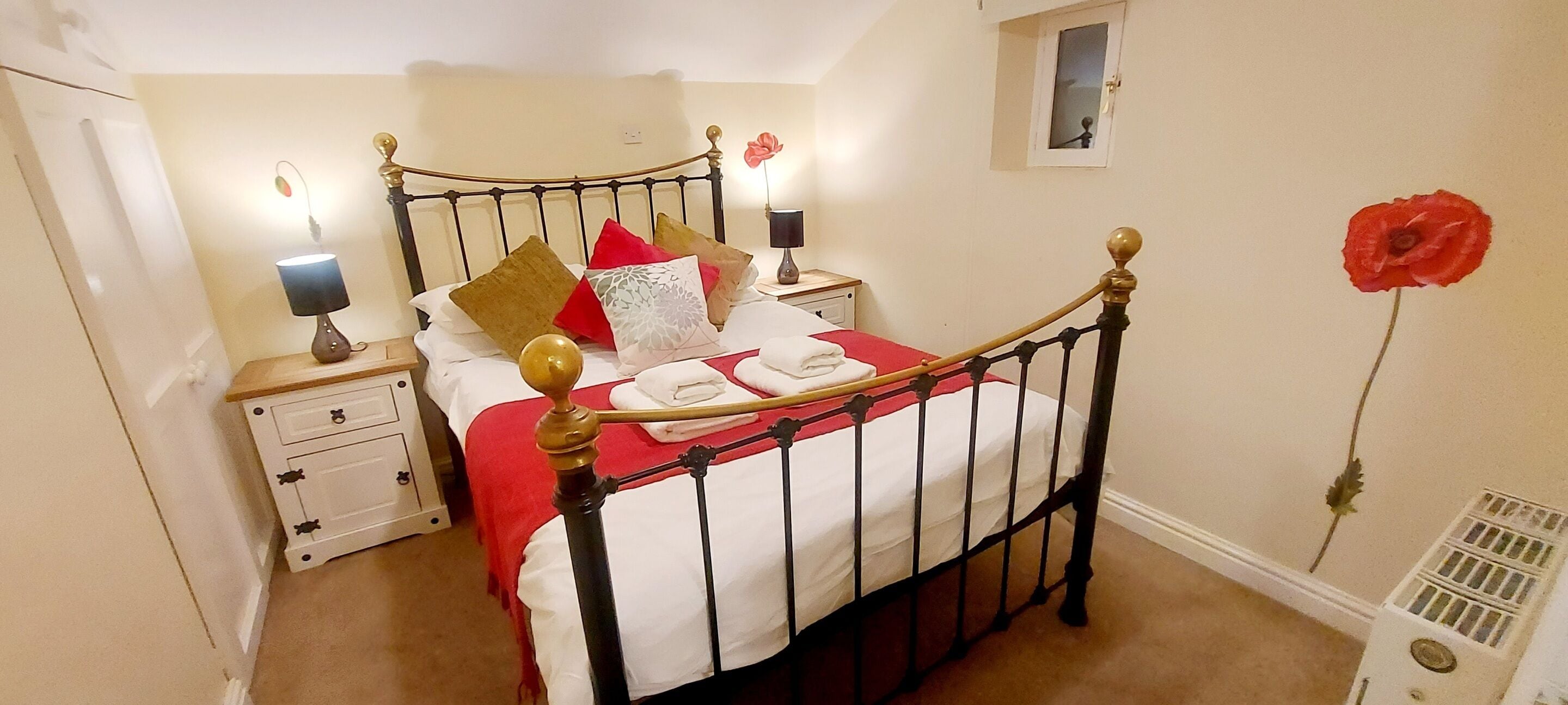 A neatly made bed with a red and white bedspread, a wooden headboard, and a nightstand with a lamp.