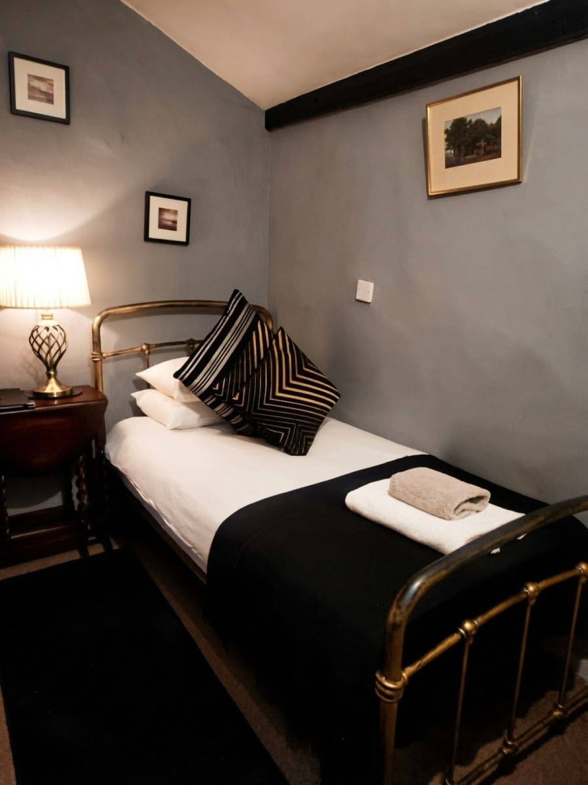 A neatly made bed with a black and white striped pillow, a white towel, and a gold-framed headboard.