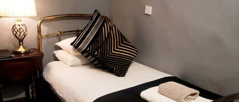 A neatly made bed with a black and white striped pillow, a white towel, and a gold-framed headboard.