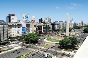 Una concurrida intersección urbana con edificios altos, un monumento destacado y varios anuncios publicitarios comerciales.
