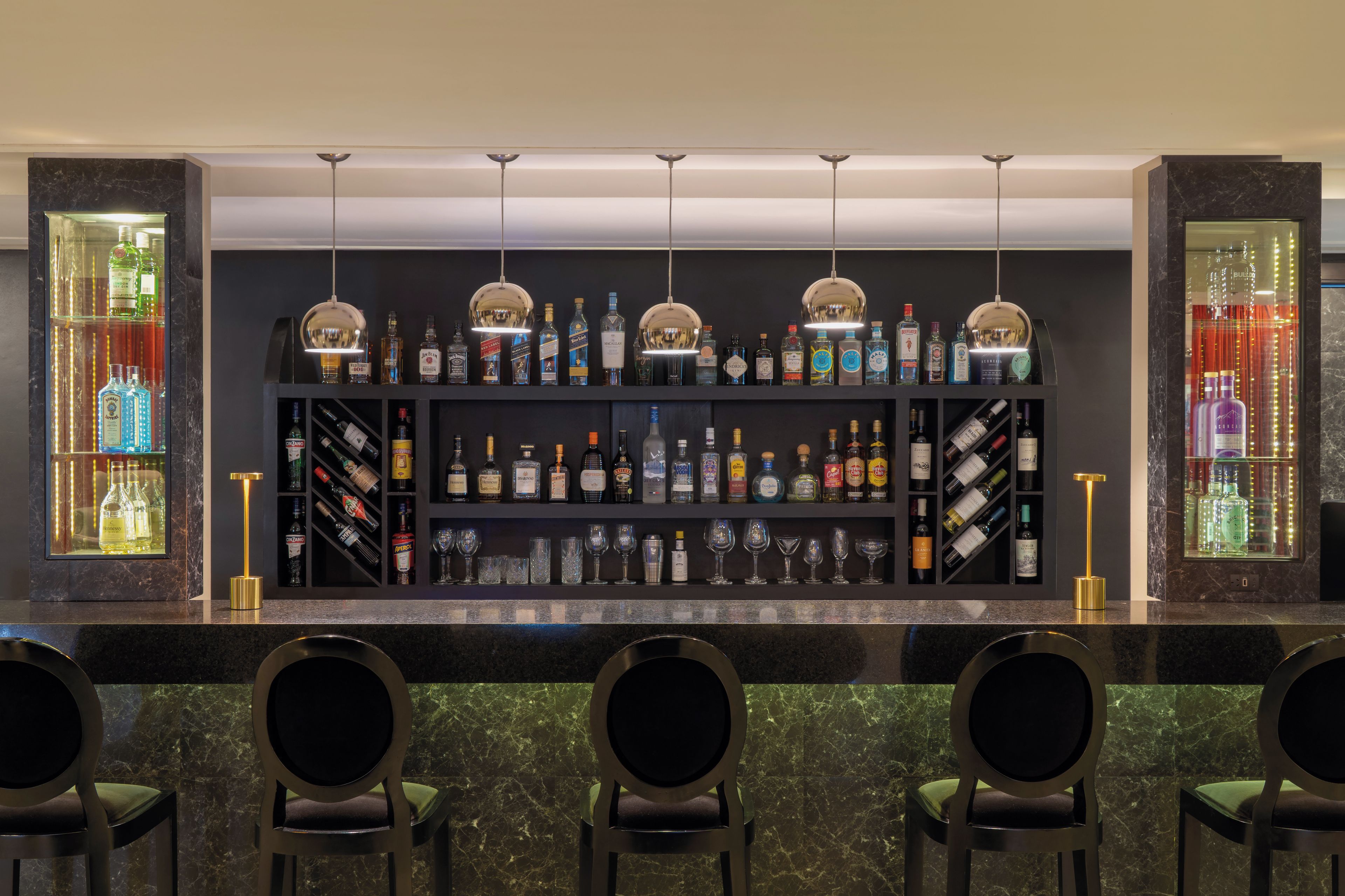 A bar area with a marble countertop, multiple shelves of liquor bottles, and three bar stools.