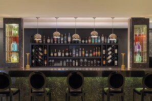 A bar area with a marble countertop, multiple shelves of liquor bottles, and three bar stools. - NH Buenos Aires Tango (Buenos Aires)