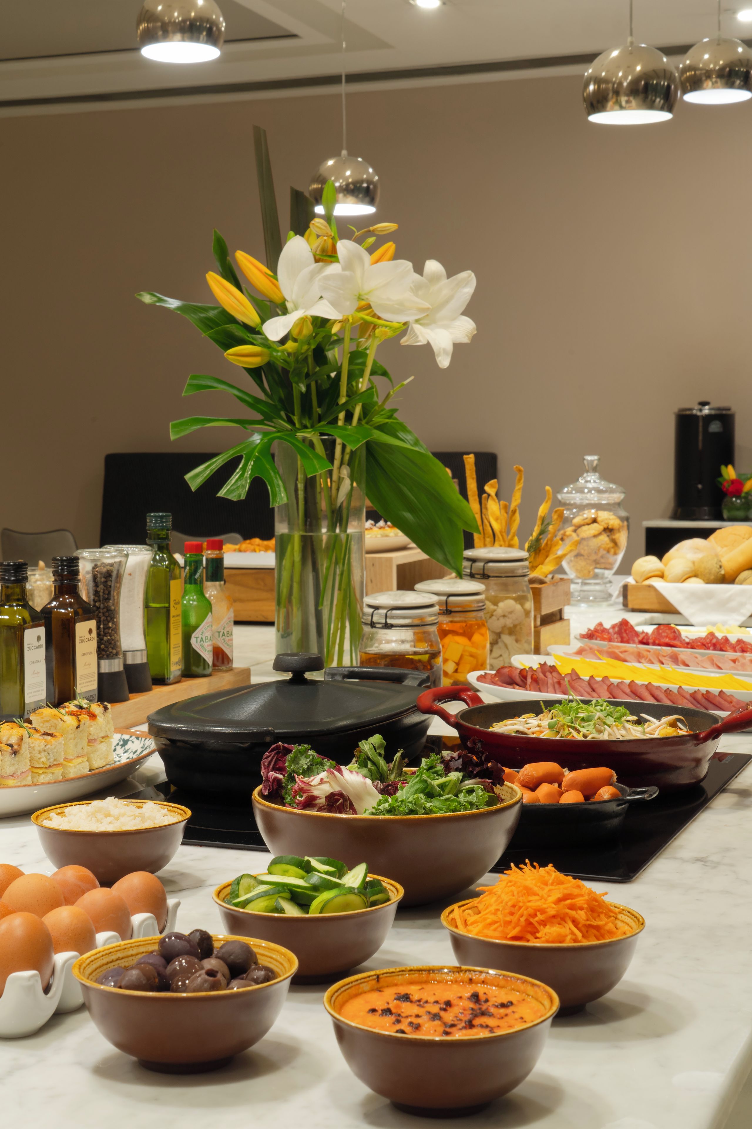 A buffet table with various food items, a vase with flowers, and a coffee machine.