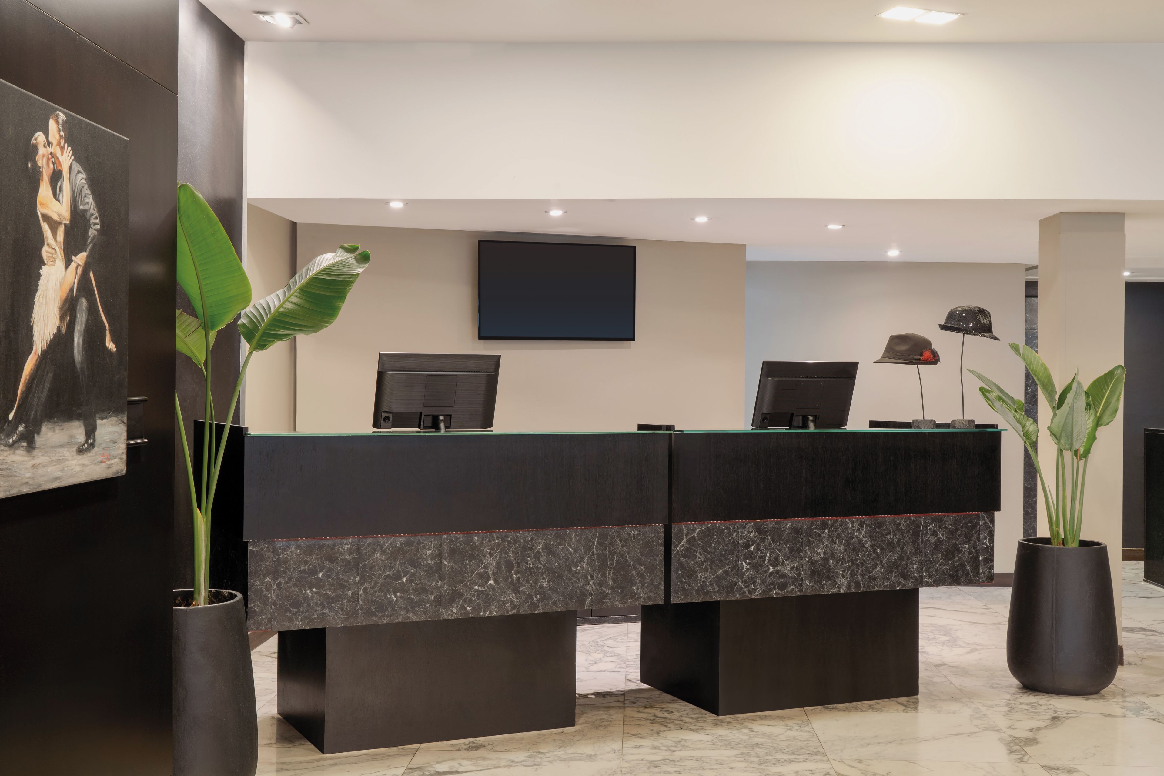 A reception desk with two computer monitors, a flat-screen TV, and potted plants.