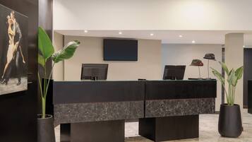 Un mostrador de recepción con dos monitores de computadora, un televisor de pantalla plana y plantas en macetas.
