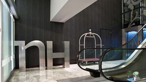A modern interior with a large 'nh' sign, a glass elevator, and a metal escalator. - NH Buenos Aires Tango (Buenos Aires)