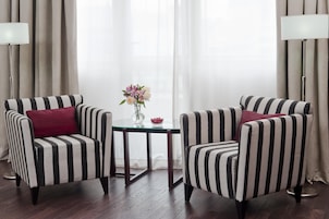 Duas poltronas listradas com almofadas vermelhas, uma pequena mesa redonda com um vaso de flores e um abajur.