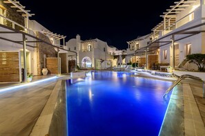 A swimming pool surrounded by white buildings with balconies, stone walls, and outdoor lighting. - La Mer Deluxe Hotel & Spa - Adults only (Santorini)