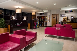 A hotel lobby with a reception desk, red seating area, and a variety of amenities including a minibar, vending machines, and a coffee station. - Roomzzz Leeds City (Leeds)
