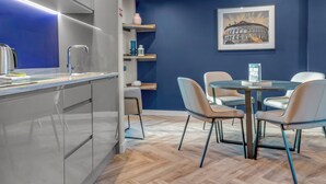 Una cocina moderna con estufa integrada, un comedor con mesa redonda y sillas, y una pared azul decorada con un cuadro enmarcado.