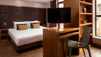 A modern hotel room with a large bed, a wooden desk, a flat-screen TV, and a bookshelf.