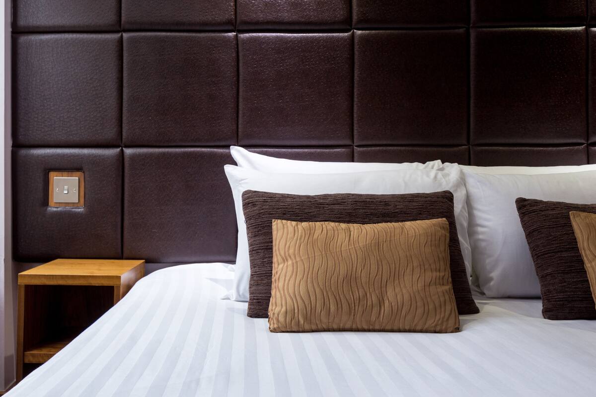 A neatly made bed with a striped white bedspread and two pillows, one white and one brown, against a dark headboard.