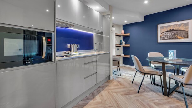 Una cocina moderna con microondas integrado, una isla iluminada en azul y un comedor con mesa y sillas.